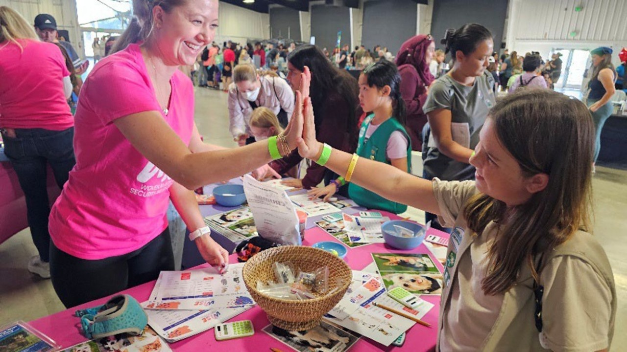 Real-World Math: A Girl Scout Cadette high-fives a volunteer from WISE (Women Investing in Security and Education) after calculating the true cost of pet ownership.